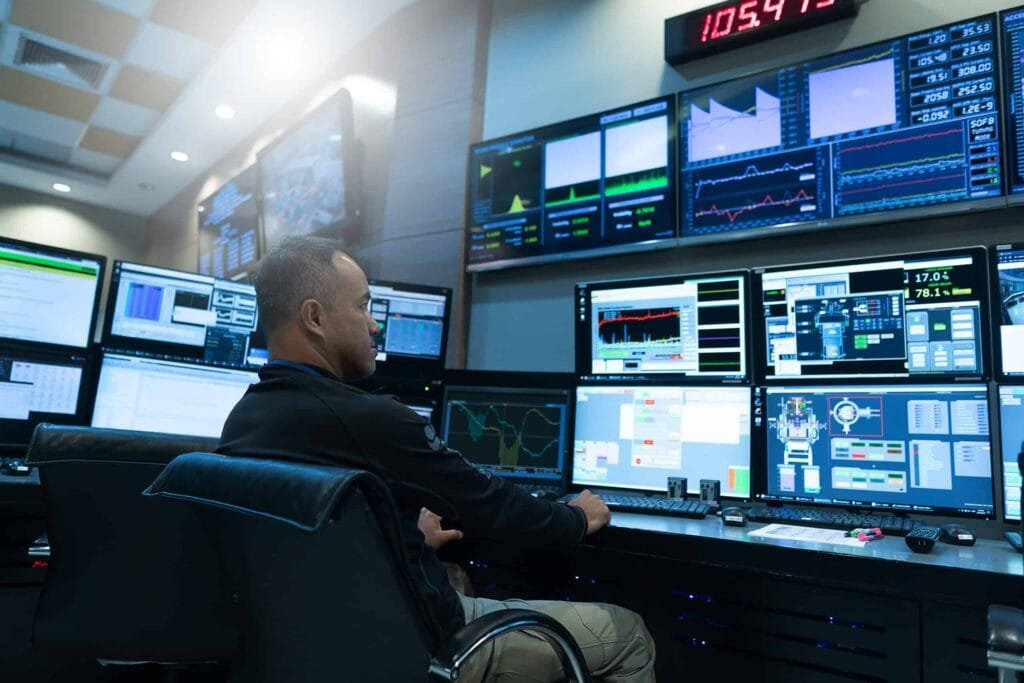 In a network operations room, a cybersecurity analyst monitors multiple screens with live system dashboards, alerts, and threat data for fast incident response.